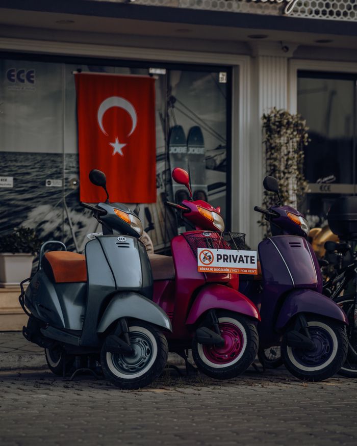 Vibrant scooters parked by a shop with a Turkish flag, showing urban street life.