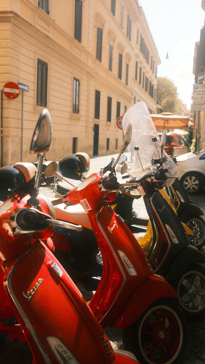 Vibrant Vespa scooters bask in sunlight on a charming street in Rome, Italy, exuding a retro vibe.